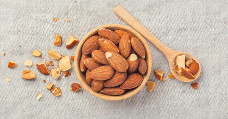 Almonds in wood bowl and spoon with broken almond on linen tablecloth background