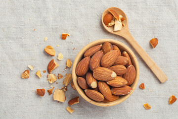 Roasted almonds in wooden bowl and spoon on linen table cloth background