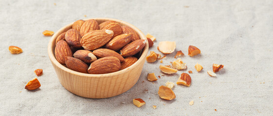 Almond nuts in wooden bowl with broken almonds on linen tablecloth background