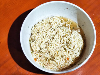 Chewy white instant noodles are held up in a white bowl, highlighting their texture and deliciousness, against the blurry background of the bowl.