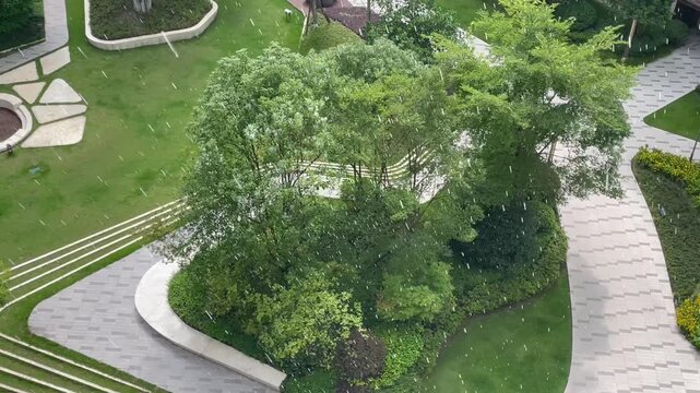 Aerial time - lapse of a sunshower in a residential garden. Begins with sunny shadows, shifts to sudden sun rain, ends with heavy rain as light fades. Shows dynamic weather over greenery and paths.