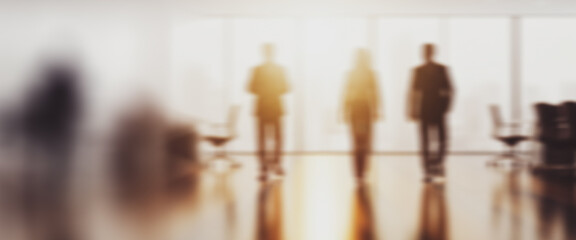 Blurred figures stand in an office with a large window and bright light.