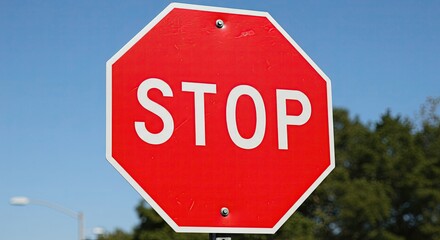 Red stop sign with white lettering against a clear blue sky backdrop