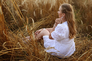 Girl in a white dress in a wheat field at sunset