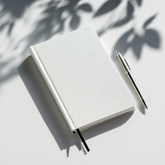 White notebook and silver pen with leaf shadows writing