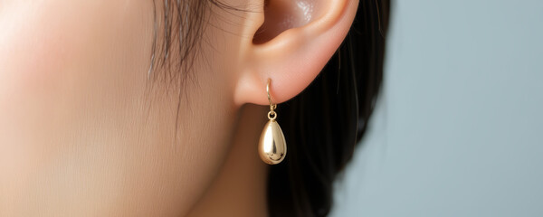 Golden drop earring hanging on ear with smooth shiny surface, elegant jewelry accessory for women, close up detail with soft background