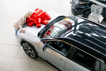 Woman Leaning on New Car with Red Bow in Dealership
