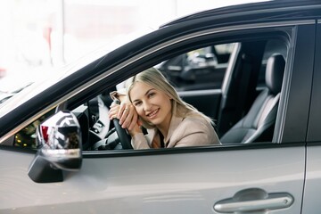 Happy business woman sitting in new car at dealership showroom