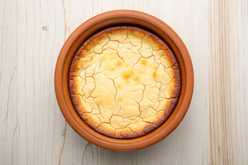Overhead view of a delicious freshly baked cheesecake in a terracotta baking dish on wooden surface