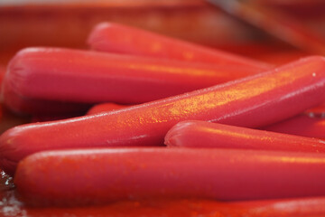 Colorful hot dogs piled on a red surface ready for grilling