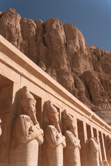 Majestic statues guarding hatshepsut temple in luxor, egypt, under a clear blue sky