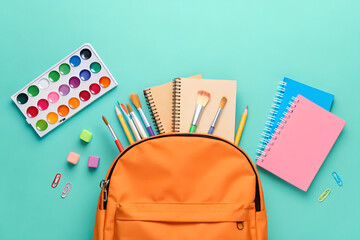 Orange backpack with school supplies including paintbrushes, notebooks, and watercolor paints