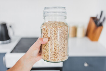 hand holding glass jar of barley in front of kitchen bokeh, cooking from scratch and having an...