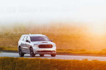 Expensive white suv crossover travels along a scenic road with lush green fields