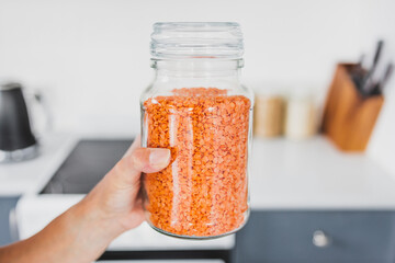 hand holding glass jar of red lentils in front of kitchen bokeh, cooking from scratch and having an...