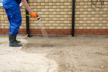 Preparing the base for pouring a concrete slab. The builder pours water on the sand for compaction.