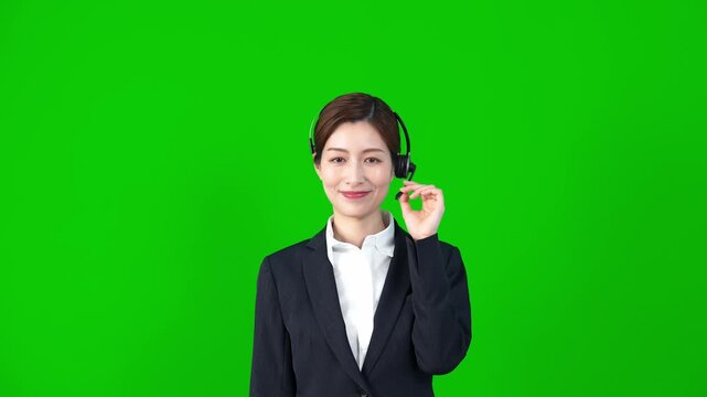 Female staff wearing a headset in front of green background for chroma key composition.