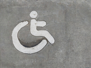 Top view of white wheelchair sign painted on textured asphalt surface, symbolizing accessibility for people with disabilities in public places, healthcare zones, and urban infrastructure