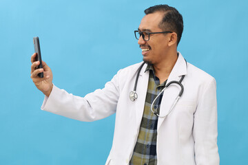 Asian adult male doctor standing wearing doctor's coat and hanging stethoscope on neck laughing...