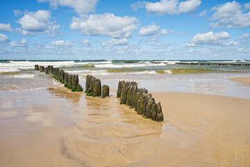 Scenic of beach on Baltic Sea - blue sky with clouds, wave sea and wooden waterbreak.