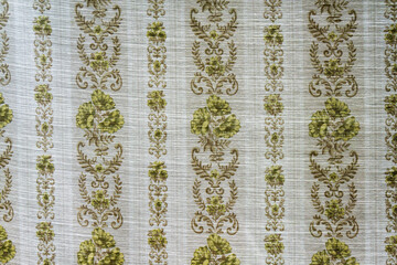 A thin textile curtain with vertical patterns of flowers and leaves in a soft pastel color. The back side is illuminated by sunlight