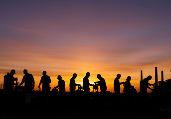 Fototapeta premium Silhouetted Workers at Sunset | Construction Crew Laboring at Dusk for Industrial and Teamwork Projects