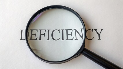The word deficiency is magnified under a magnifying glass, representing a lack, shortage, or inadequacy in something