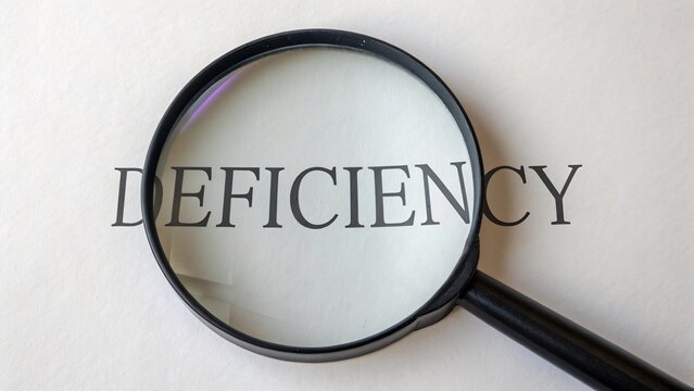 The word deficiency is magnified under a magnifying glass, representing a lack, shortage, or inadequacy in something
