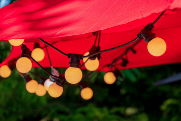 Glowing orbs hang from a red canopy, casting a warm light in a tranquil garden at sunset