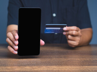 Close-up of hands using phone and bank card for digital transaction, e-commerce interface.