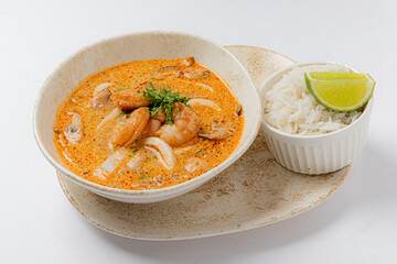 A vibrant bowl of seafood curry, brimming with shrimp, served alongside rice and lime wedges