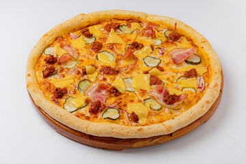 A scrumptious pizza featuring ham, pickles, melted cheese, and crispy meat on a wooden serving tray