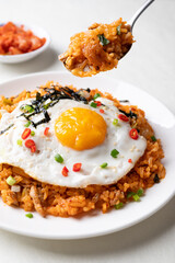 Kimchi fried rice with fried egg, pork, sesame seed, chili, spring onion and seaweed on white plate and eating, Korean food