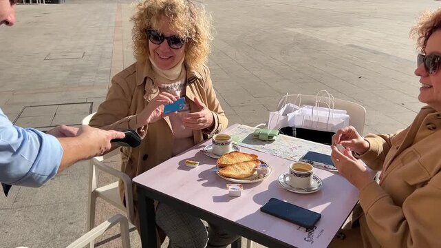 Middle-aged woman paying with credit card at outdoor caf&eacute; after breakfast during a relaxing morning in a Spanish village square