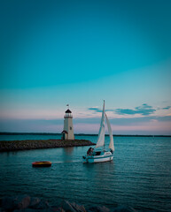 lighthouse at sunset with sailboat 