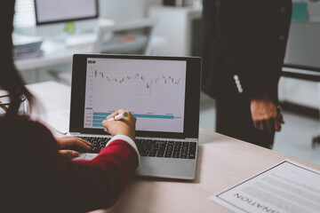 Businesswoman pointing at financial charts on laptop screen while a colleague observes, discussing...