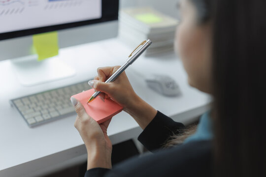 Focused individual writing on sticky notes at a modern workspace, with a computer and office supplies in the background