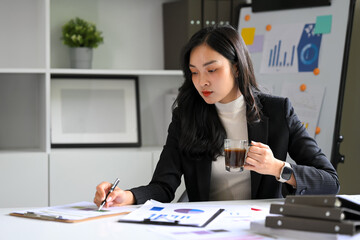 Businesswoman holding a cup of coffee and reviewing documents in a bright modern office