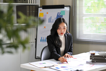 Asian businesswoman reviewing financial reports and data sheets at her desk
