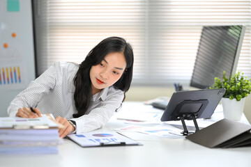 Office worker analyzing financial charts while reaching for stacked documents during work