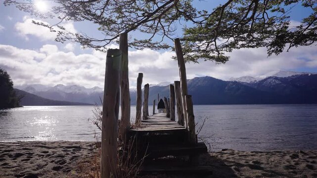 Mother and daughter walking on a rustic wooden and peaceful pier at Lago Traful, Argentina.