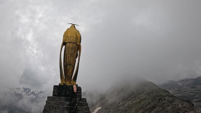 Golden Madonna statue stands at Monte Moro Pass in the Italian Alps near Macugnaga under a cloudy sky.