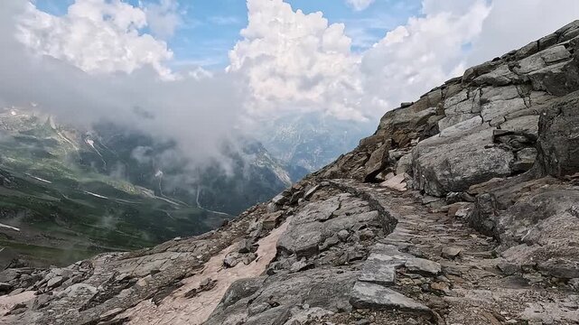 Rugged alpine path curves along a rocky cliff edge under dramatic clouds near Colle del Turlo, Italian Alps.