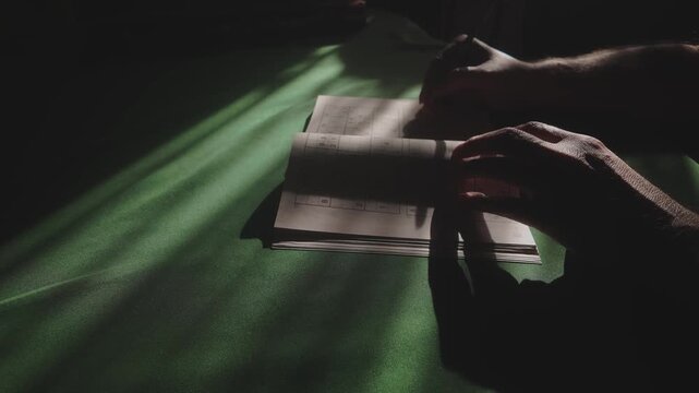 Puzzle solver in study room shadows concentrates on Soduku book