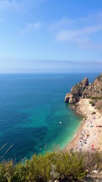 Tourists are swimming and sunbathing at Cala Moraig beach, a beautiful cove with crystal-clear turquoise waters located in Benitachell, Alicante, Spain, during a sunny summer day