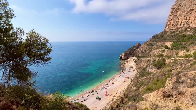 Tourists are swimming and sunbathing at Cala Moraig beach, a beautiful cove with crystal-clear turquoise waters located in Benitachell, Alicante, Spain, during a sunny summer day