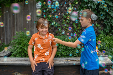 Two boys having fun and playing with bubbles in  backyard garden
