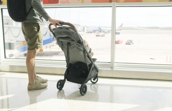 Dad pushing stroller at airport looks out window at airplanes