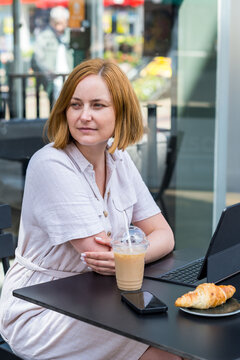 Middle age woman drinking coffee and working on laptop at a caffe