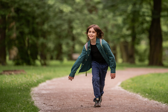 Carefree smiling boy running along path in green park